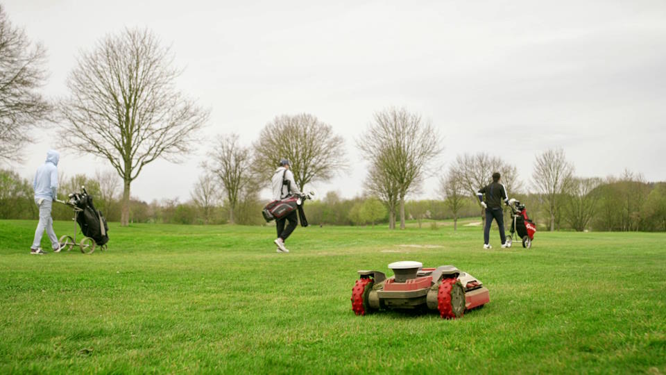 Rasenmäherroboter von Kress im Vordergrund, im Hintergrund laufen Golfer durch das Bild